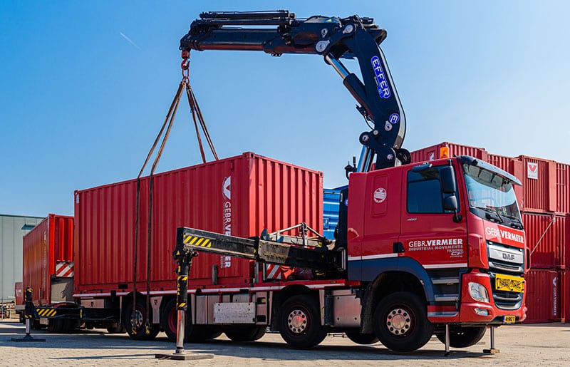 Flachbett-Trailer mit Container und Kranentladung